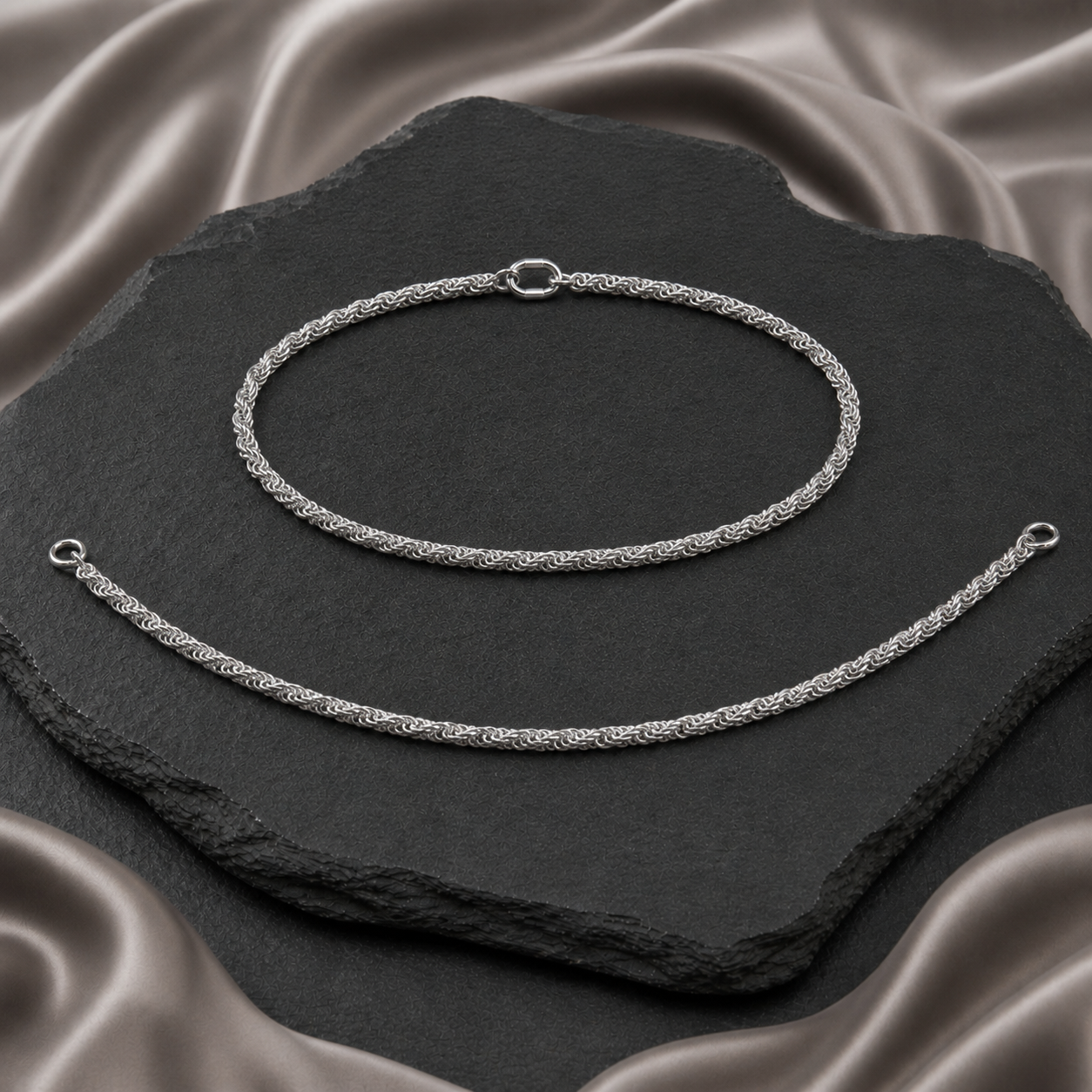 Pair of polished silver payals with a twisted rope link pattern displayed on charcoal stone